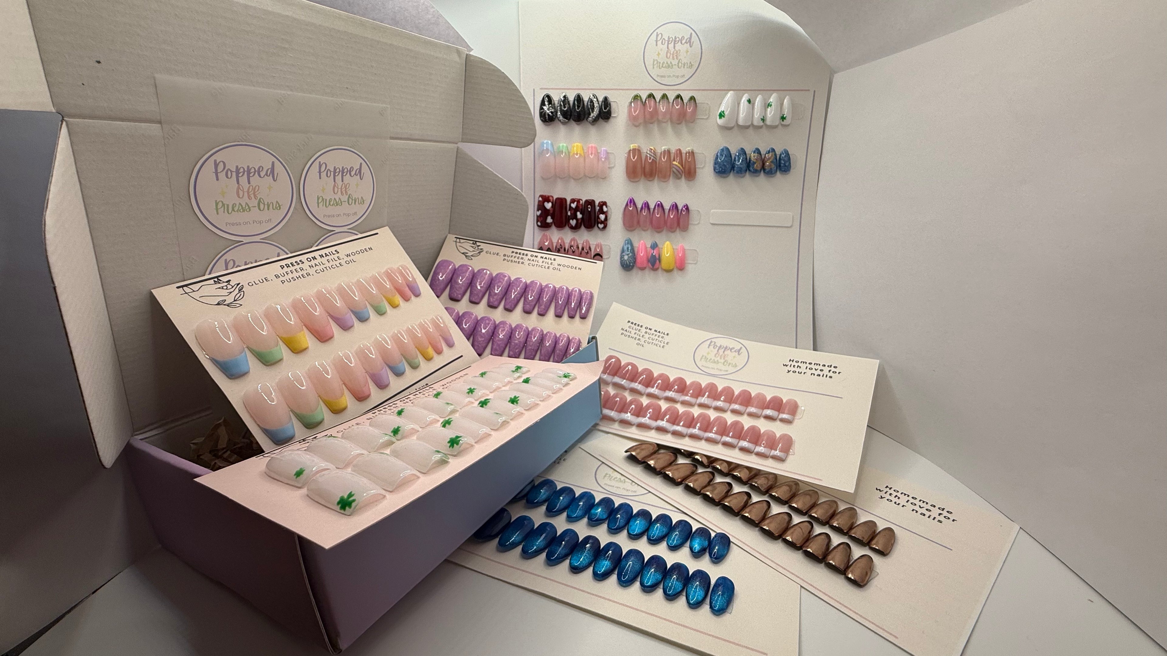 Display of false nail sets in various colors with open boxes on a neutral background