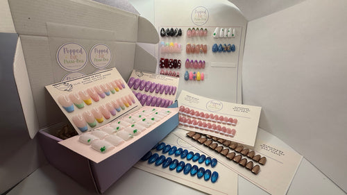 Display of false nail sets in various colors with open boxes on a neutral background