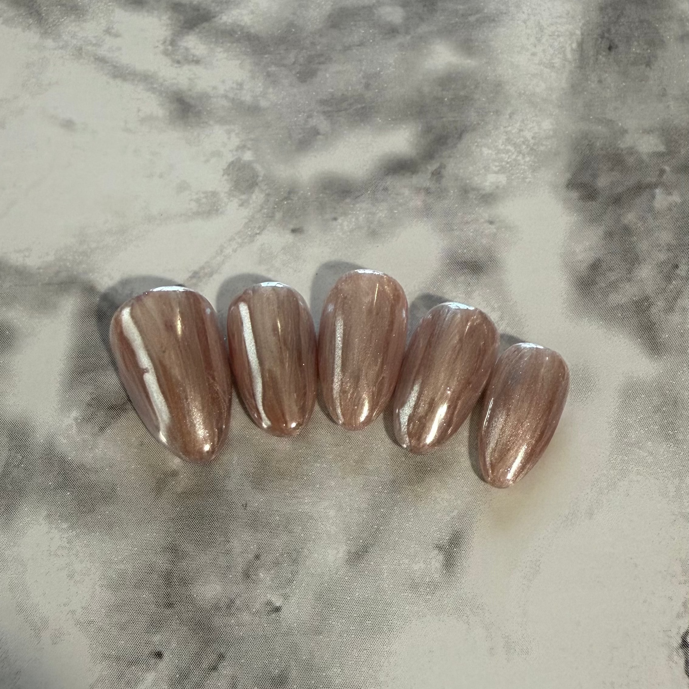 Shell inspired nails that are pink and cream with a stripy design and a shimmery chrome top