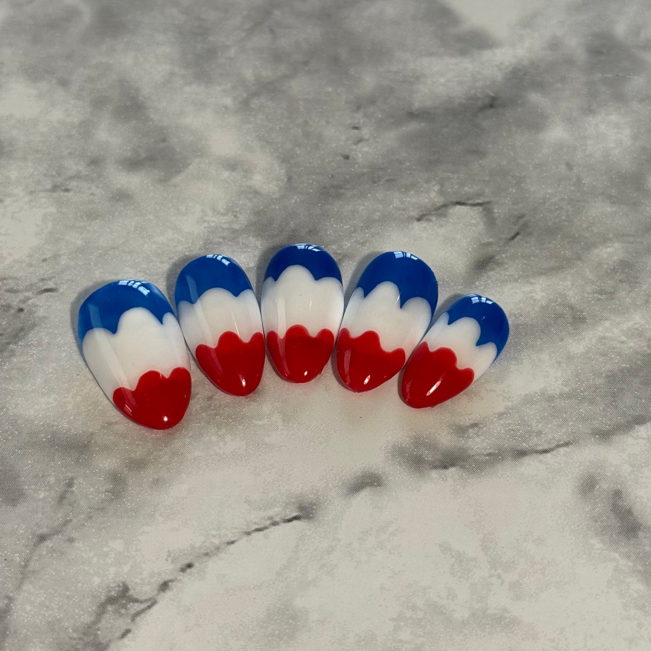 Nail art with red, white, and blue design that is a swirly to imitate a melting bomb pop