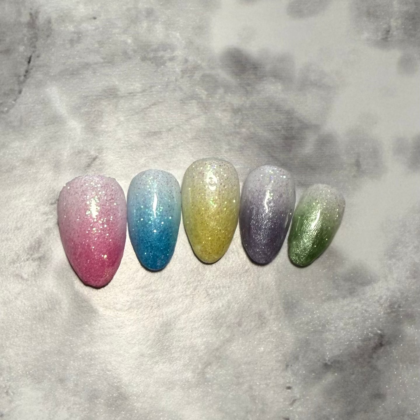 Five glittery almond shaped nails that are pink, blue, yellow, purple, and green made to look like snow cones 