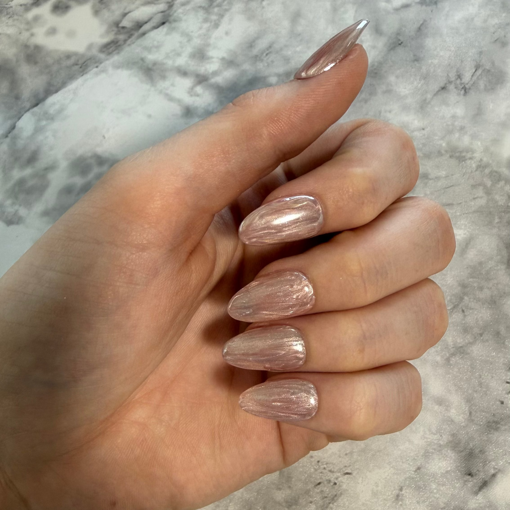 Shell inspired nails that are pink and cream with a stripy design and a shimmery chrome top on a hand