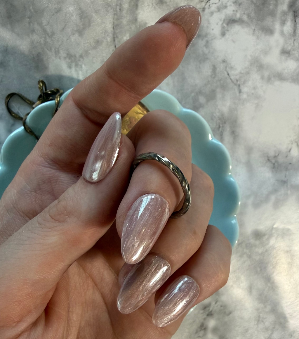 Shell inspired nails that are pink and cream with a stripy design and a shimmery chrome top on a hand holding a ring