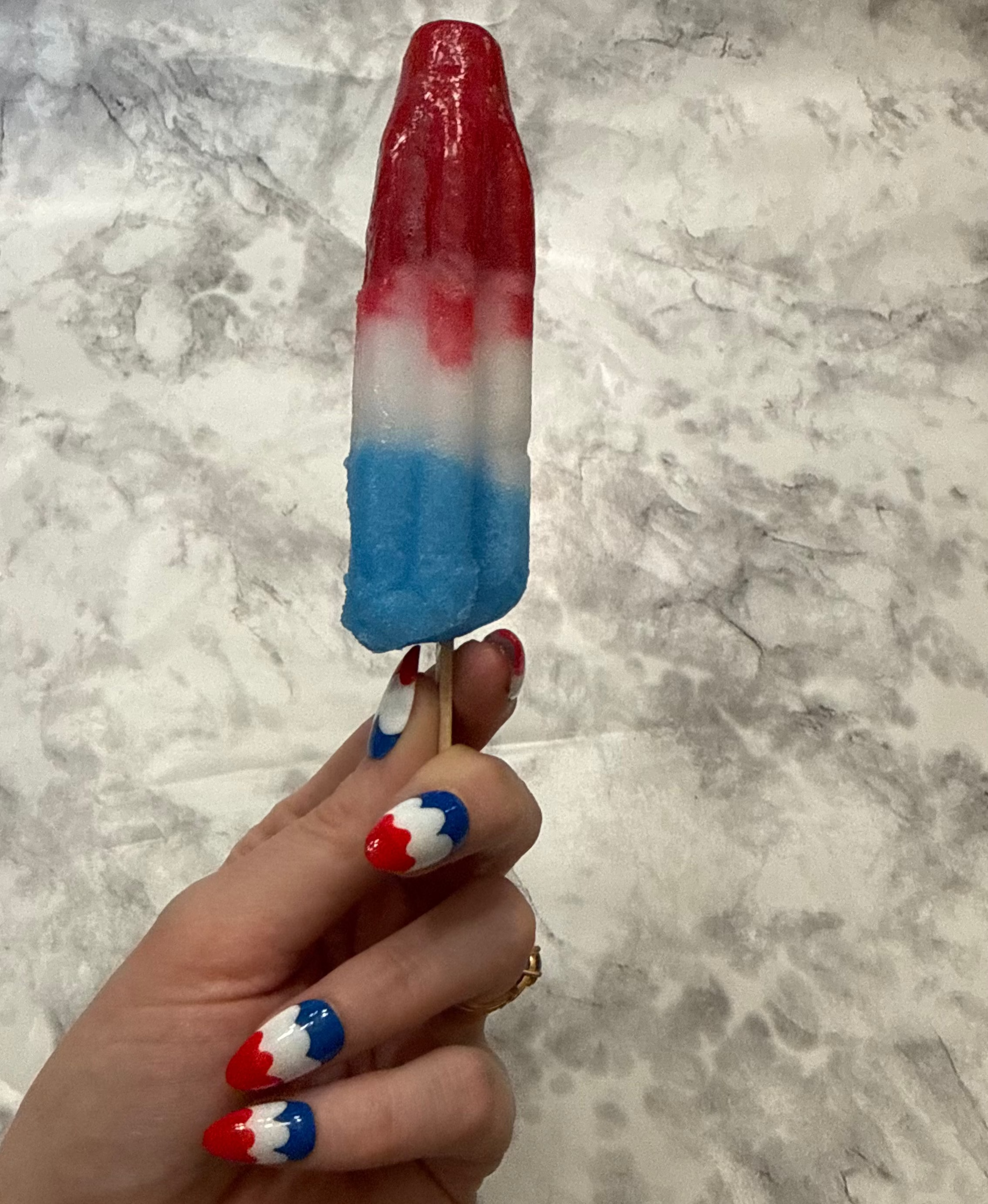 Nail art with red, white, and blue design that is a swirly to imitate a melting bomb pop on a hand holding a melting bomb pop